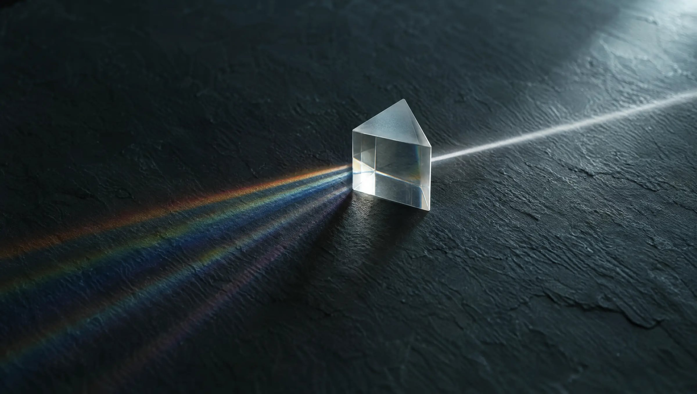 A glass prism splitting one beam of light into several on a dark surface