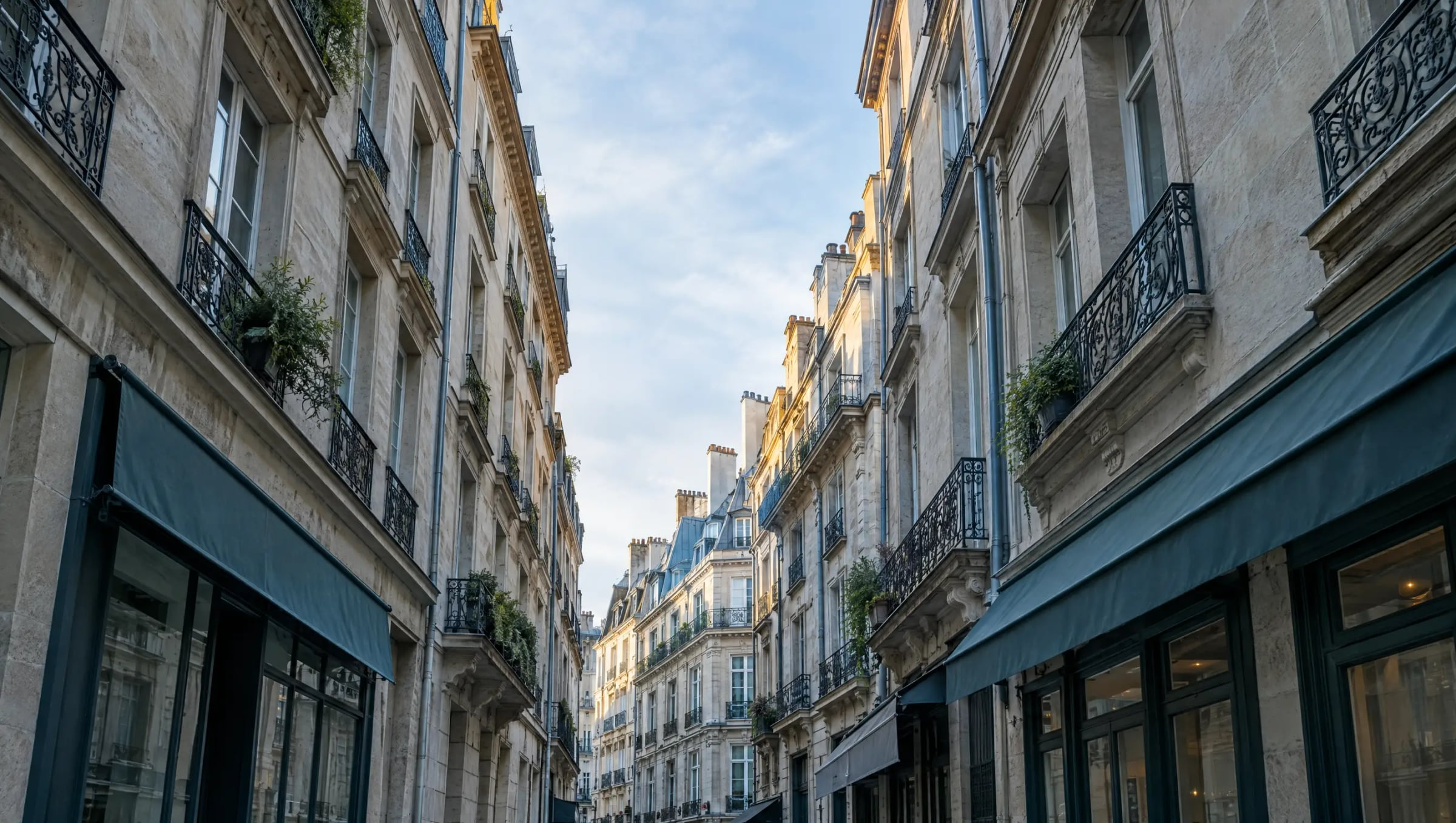 Looking up a narrow European street of stone facades, balconies and restaurant awnings