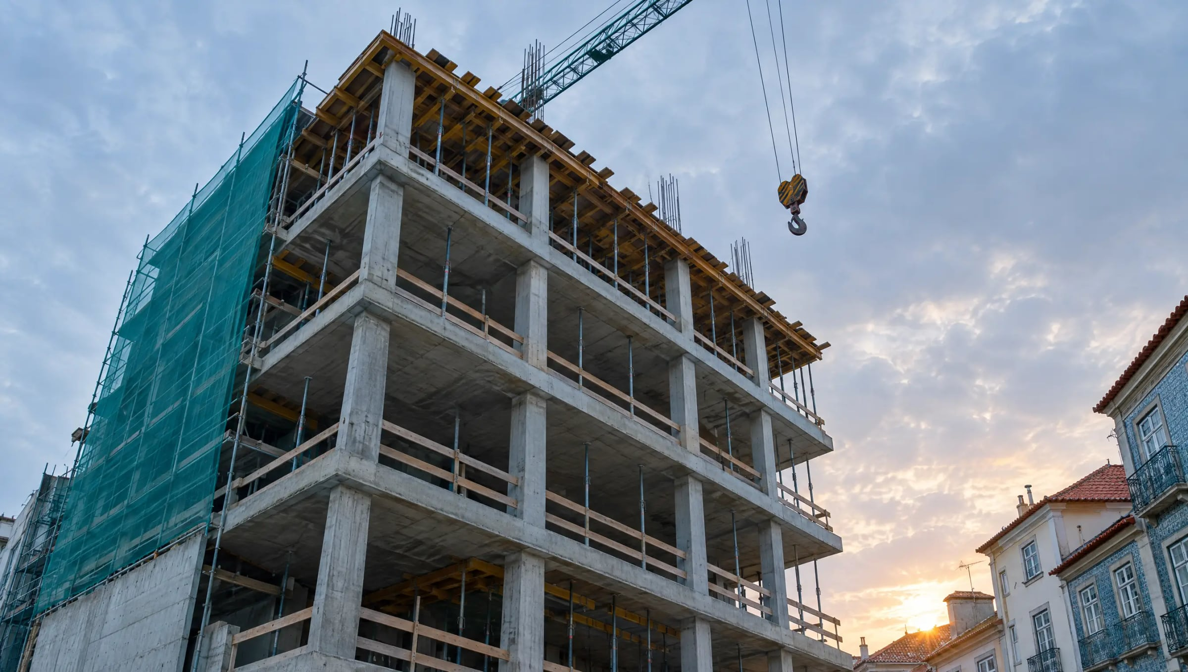 Looking up at a concrete building under construction beside old tiled houses