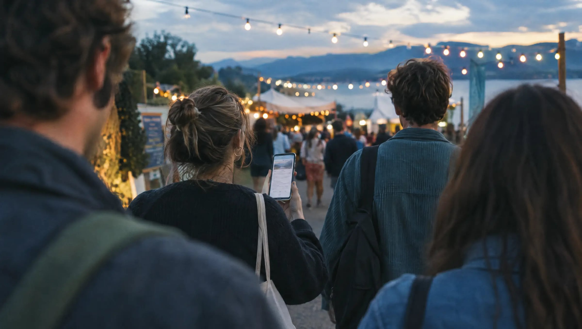 Friends walking towards an outdoor event at dusk under string lights