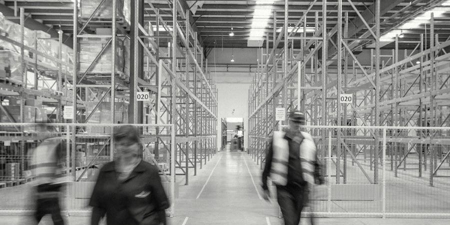 Warehouse staff walking between high pallet racks